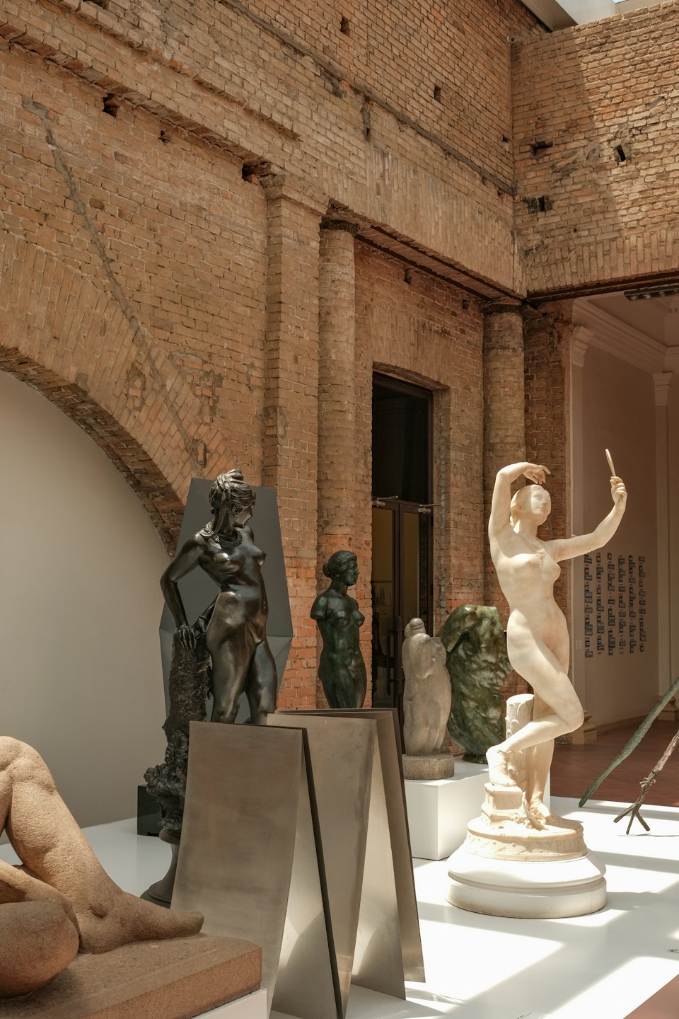 Skulpturen von Menschen in einer sonnendurchfluteten Kunstgalerie mit Ziegelwänden.